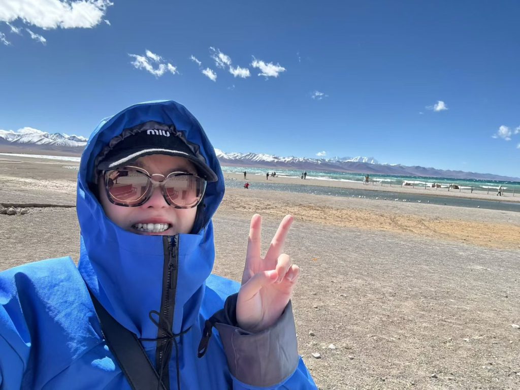 Namtso Lake Travel Guide: Lake in the Sky 8 Nicole in a blue jacket smiling and making a peace sign at Namtso Lake