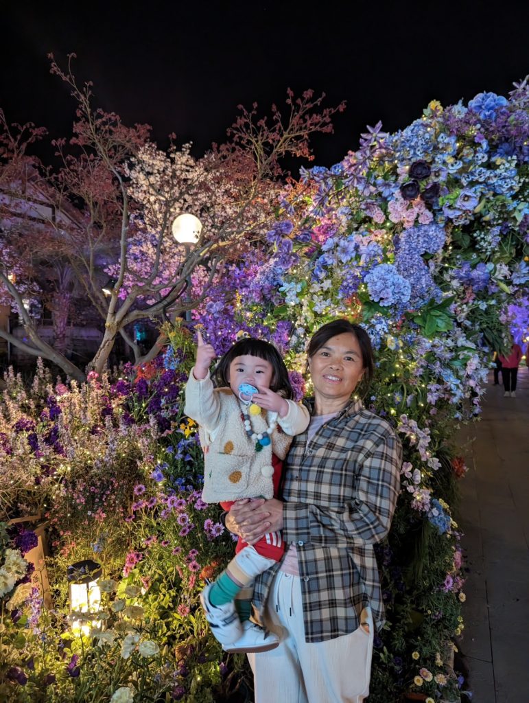 Wuxi Nianhua Bay: A Peaceful Zen Town Blending Tang-Song Architecture and Jiangnan Charm 15 Grandmother and child at the night flower display, glowing in vibrant colors.