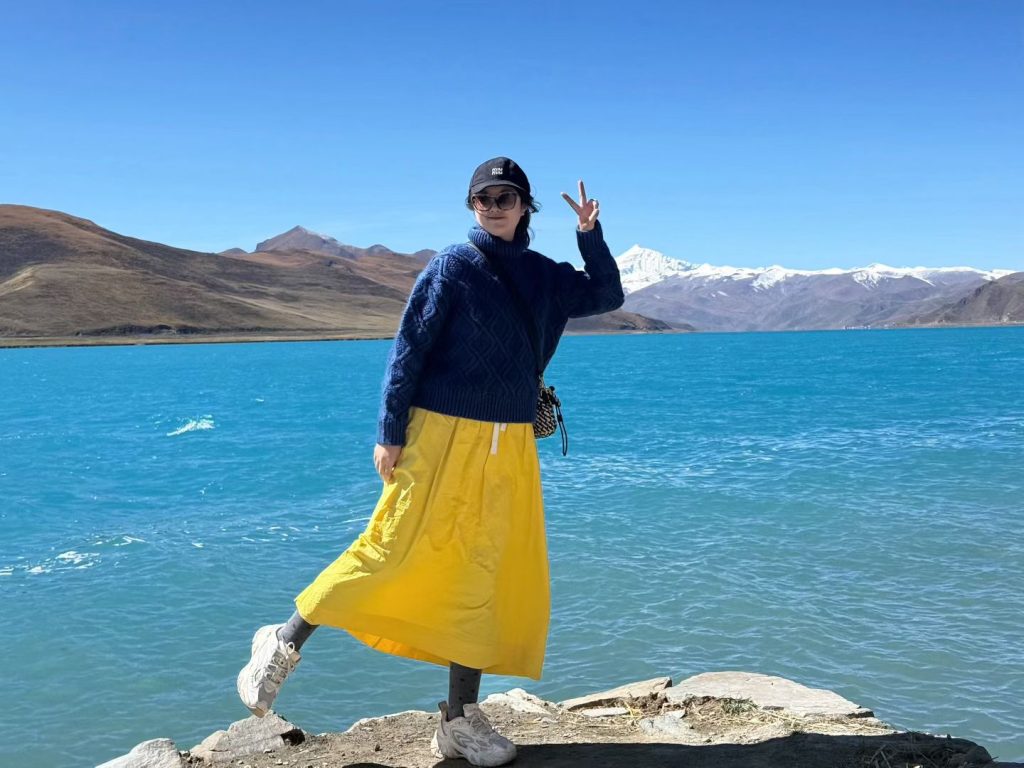 Nicole posing at Yamdrok Lake with mountains behind her