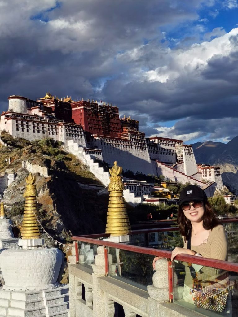 Potala Palace Lhasa: History, Visiting Tips & Best Time to Go 8 Visitor smiling near golden stupas with Potala Palace in the background under dramatic clouds.