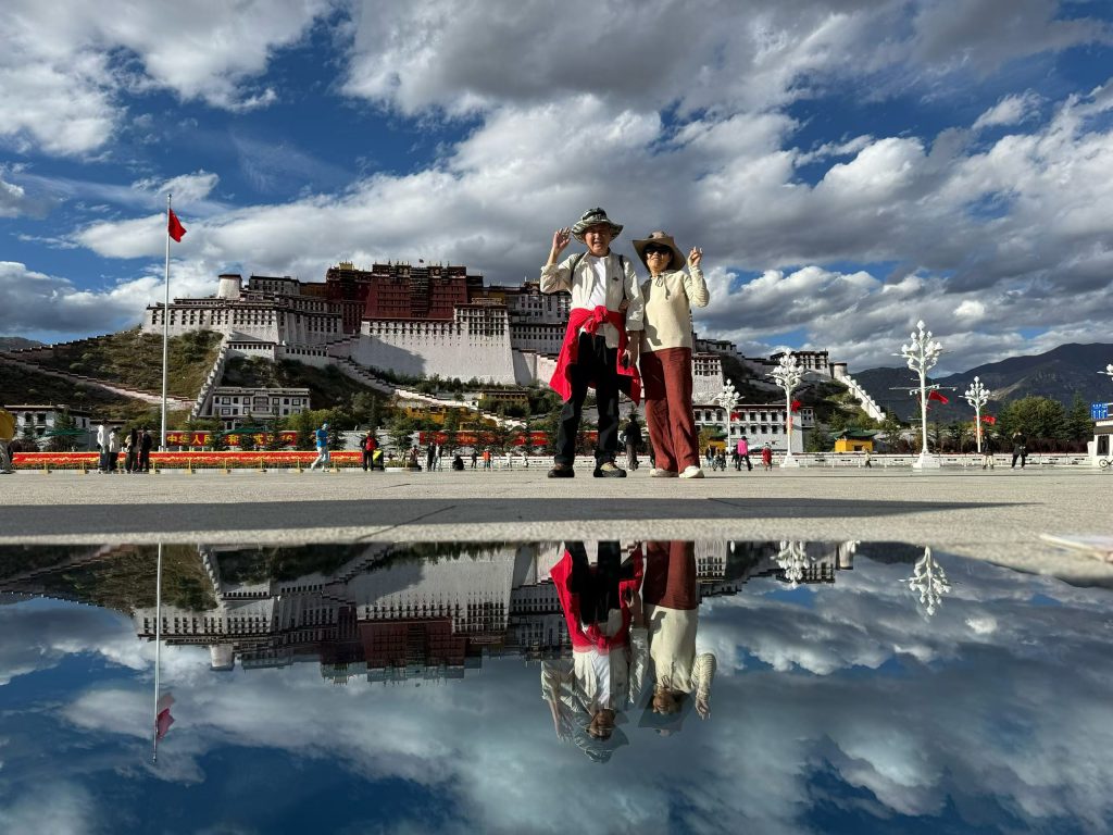 Potala Palace Lhasa: History, Visiting Tips & Best Time to Go 7 Two travelers posing happily at Potala Palace Square with a stunning mirrored reflection of the palace and sky.