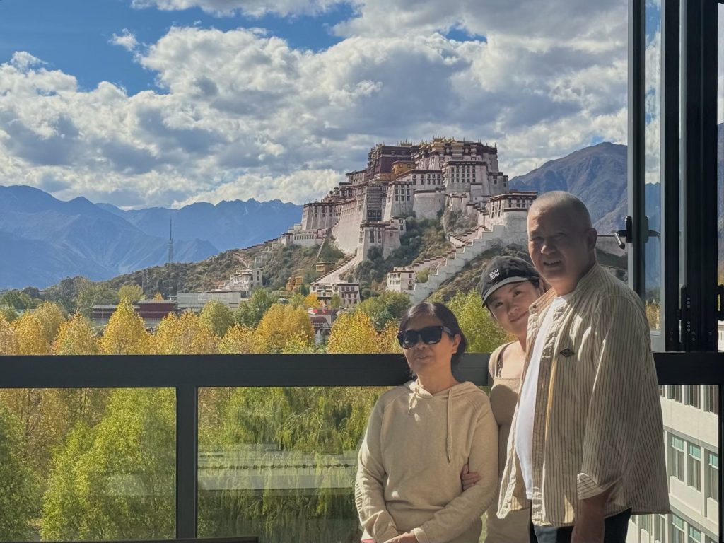 Potala Palace Lhasa: History, Visiting Tips & Best Time to Go 9 Family posing by a hotel window with Potala Palace and Himalayan mountains in the background.