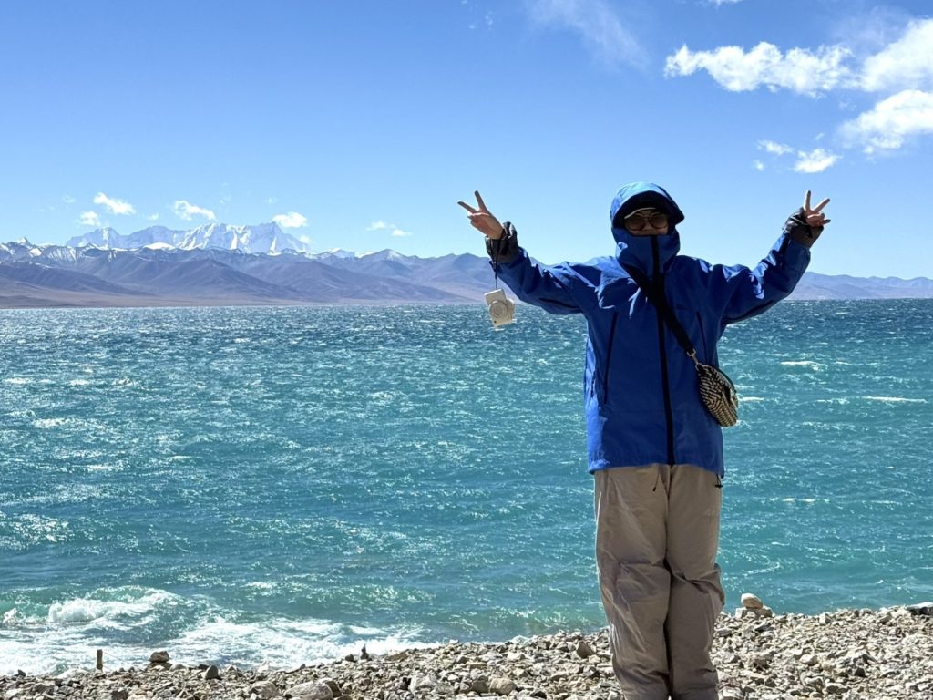 How to Plan a Trip to Tibet? 10 Standing by the windy shores of Lake Namtso with snow-covered mountains in the background