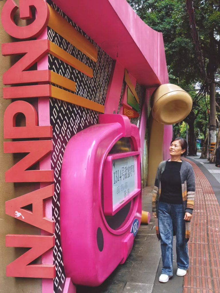 Woman standing beside a large pink retro telephone installation on Super 80 Street in Chongqing.