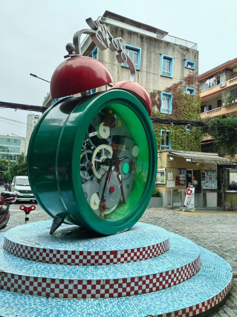 Large green retro alarm clock sculpture with exposed gears on Super 80 Street, Chongqing.