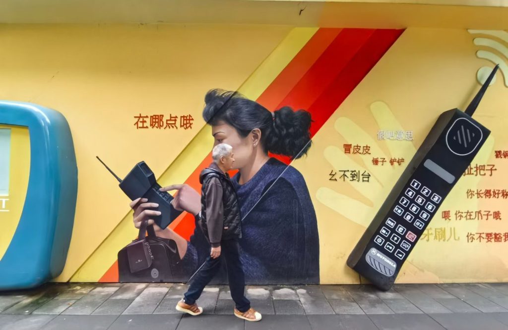 Man walking in front of a colourful 1980s-style mural featuring an old mobile phone.