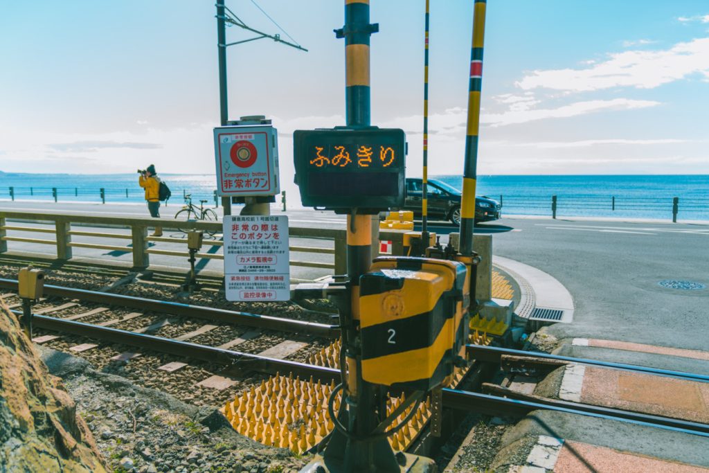 Kamakurakokomae Station: Visiting the Iconic Slam Dunk Crossing by the Sea 10 Close-up of the yellow and black railway crossing lights at Kamakurakokomae Station with the sea behind.