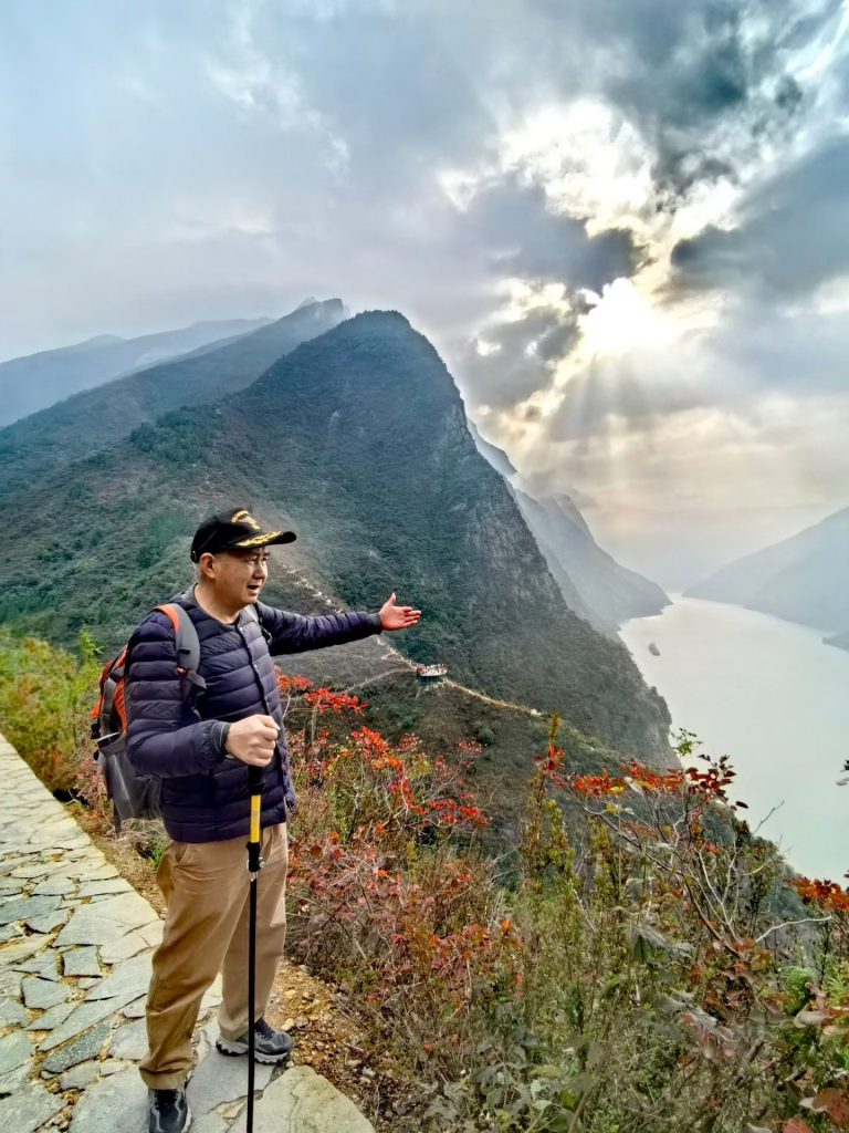 Hiking the Three Gorges Summit in Wushan: Stunning Views & Autumn Colors 8 Hiker pointing toward the sunlit ridges of Wu Gorge as rays break through the clouds at the Three Gorges Summit.