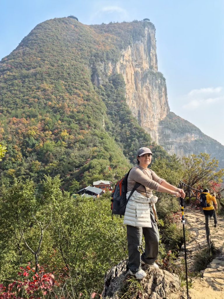 Hiking the Three Gorges Summit in Wushan: Stunning Views & Autumn Colors 7 Woman standing on a viewpoint rock with the dramatic cliff walls of Wushan rising sharply behind her.