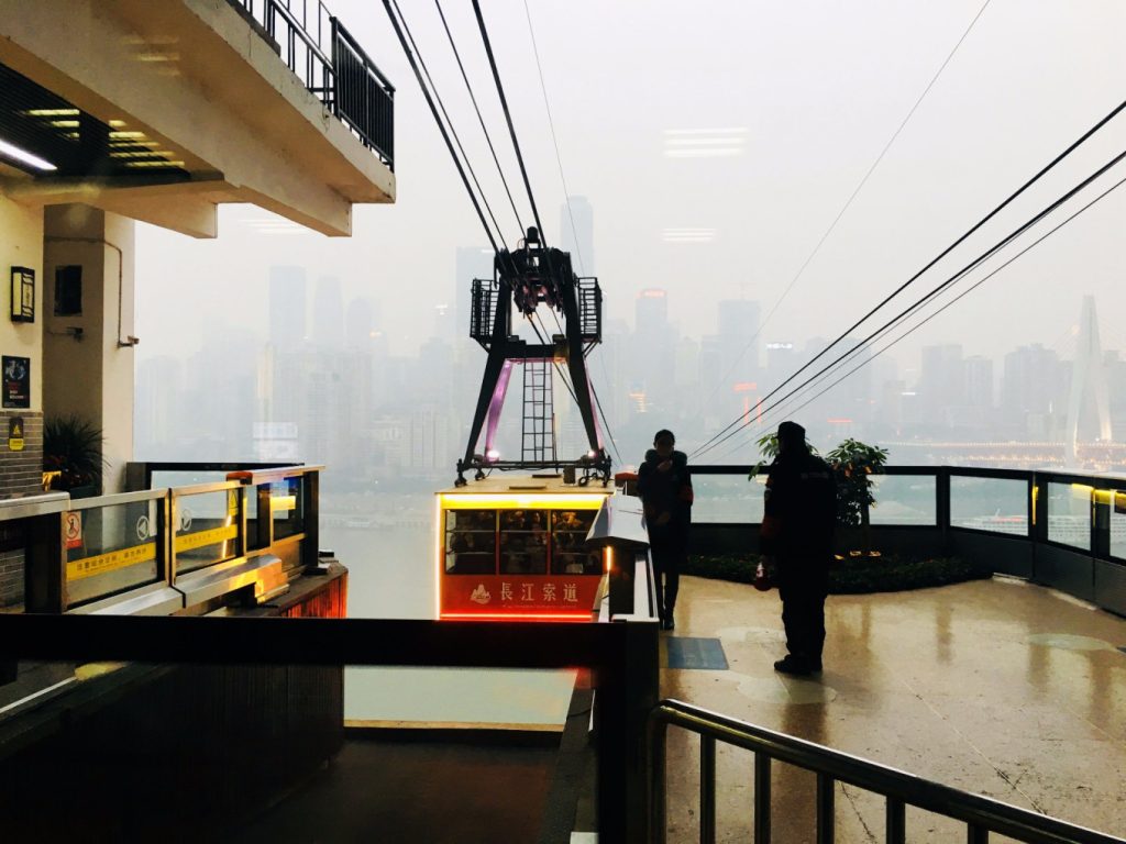 Yangtze River Cableway, Chongqing – Flying Over the Yangtze River 7 Cable car departing from the Yangtze River Cableway station with Chongqing skyline visible across the river.