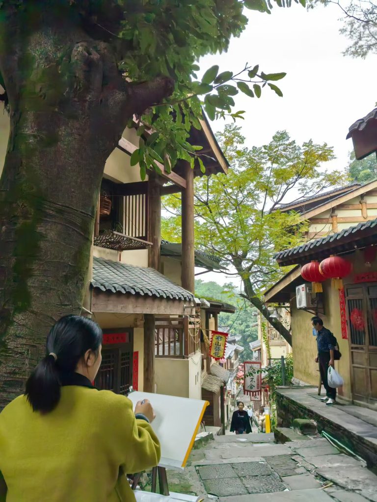 Local artist sketching a traditional Chongqing hillside street lined with wooden houses