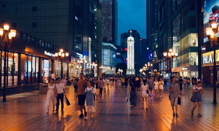 Busy pedestrian shopping street in a Chinese city at night with illuminated storefronts and crowds walking