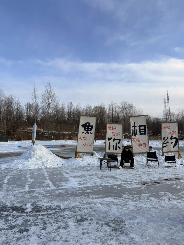 Frozen river ice fishing area with tall Chinese banners and chairs under a blue winter sky