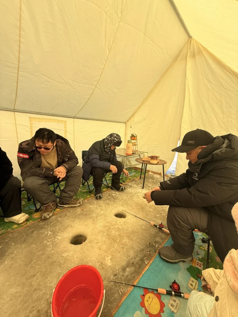 Ice fishing tent interior with multiple fishing holes and people sitting close together on mats