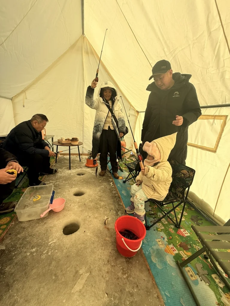 Inside the tent, an adult lifts a fish on a line while a child sits holding a fishing rod