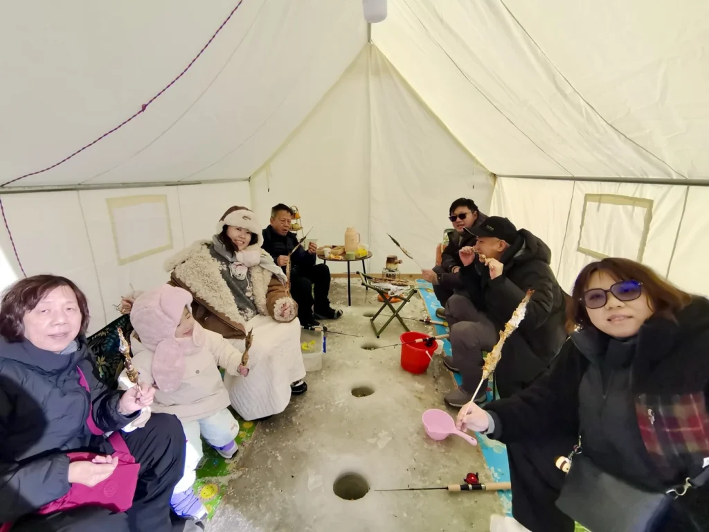 Group photo inside the ice fishing tent with family holding grilled fish skewers and ice holes visible