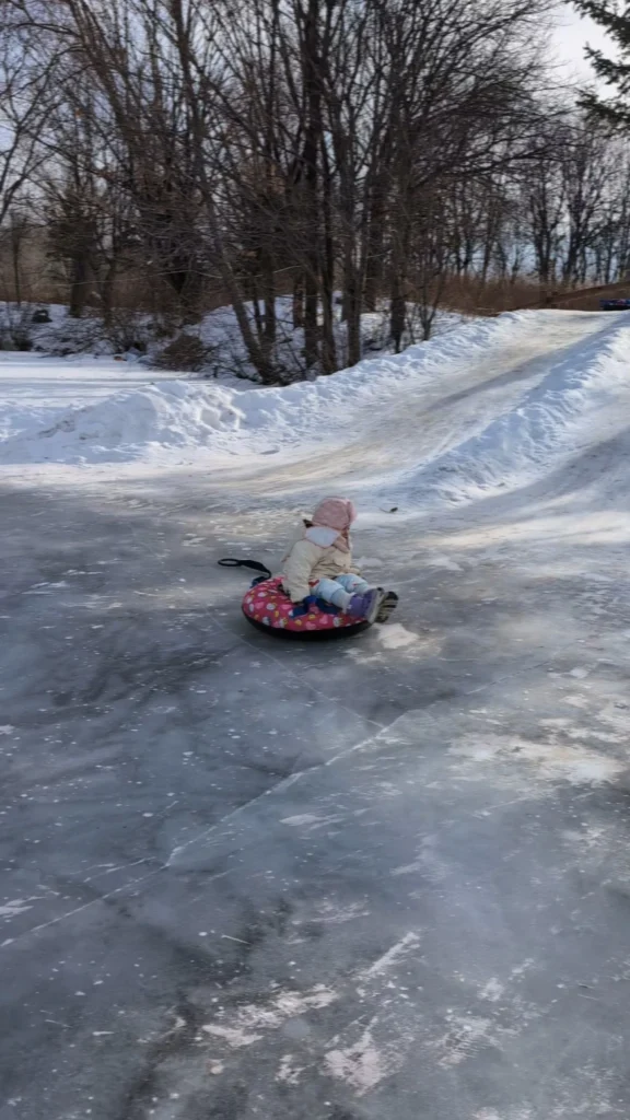 Child sitting on an inflatable snow tube sliding on a frozen track surrounded by snowbanks