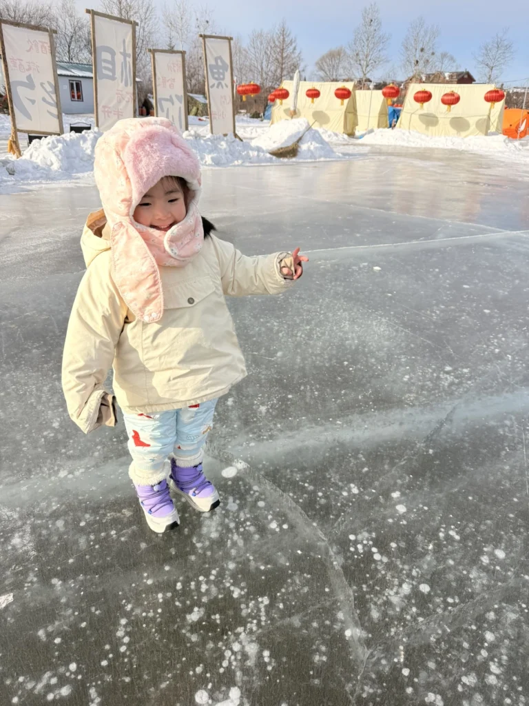 Child standing on clear frozen ice with visible air bubbles, winter tents and lanterns behind