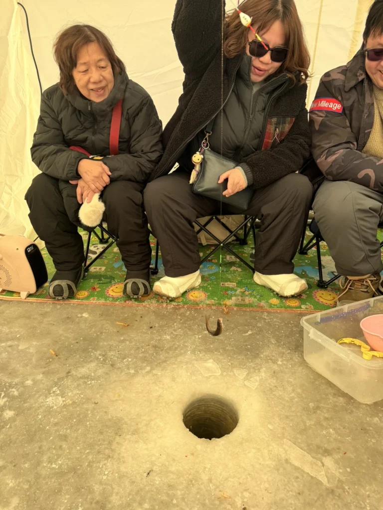 Inside an ice fishing tent with family seated around a drilled hole in the ice