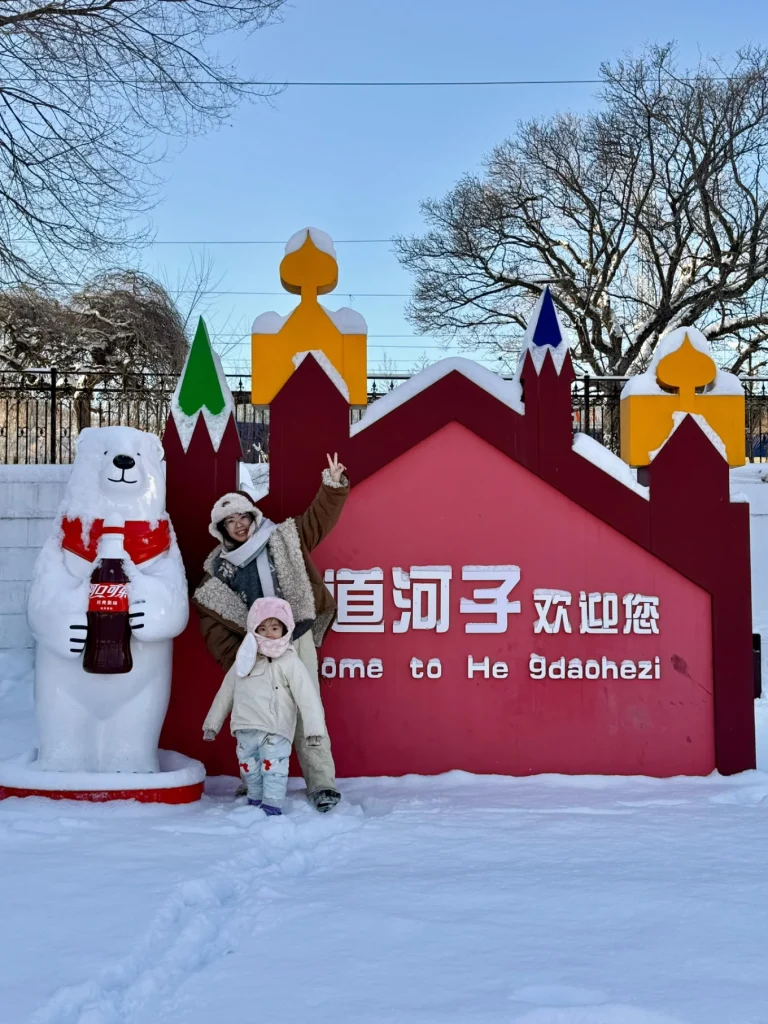 Hengdaohezi 1-Day Trip: Snowy Railway Town Near Harbin Travel Guide 5 Family photo at Hengdaohezi town entrance in winter, standing in front of the “Welcome to Hengdaohezi” sign surrounded by snow and Russian-style architecture.