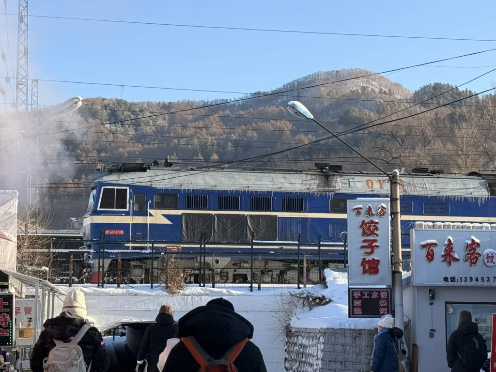 Vintage blue train at Hengdaohezi Railway Museum in winter, with snow-covered mountains behind the historic railway town.
