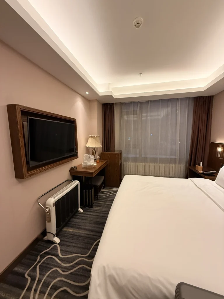 Harbin hotel room interior with bed, desk, wall-mounted TV, and portable heater for winter stays