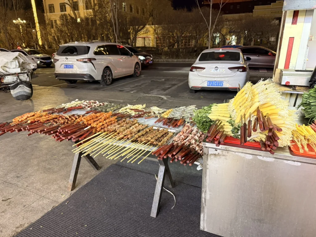 Street barbecue stall in Harbin with large skewers of meat and vegetables displayed outdoors at night