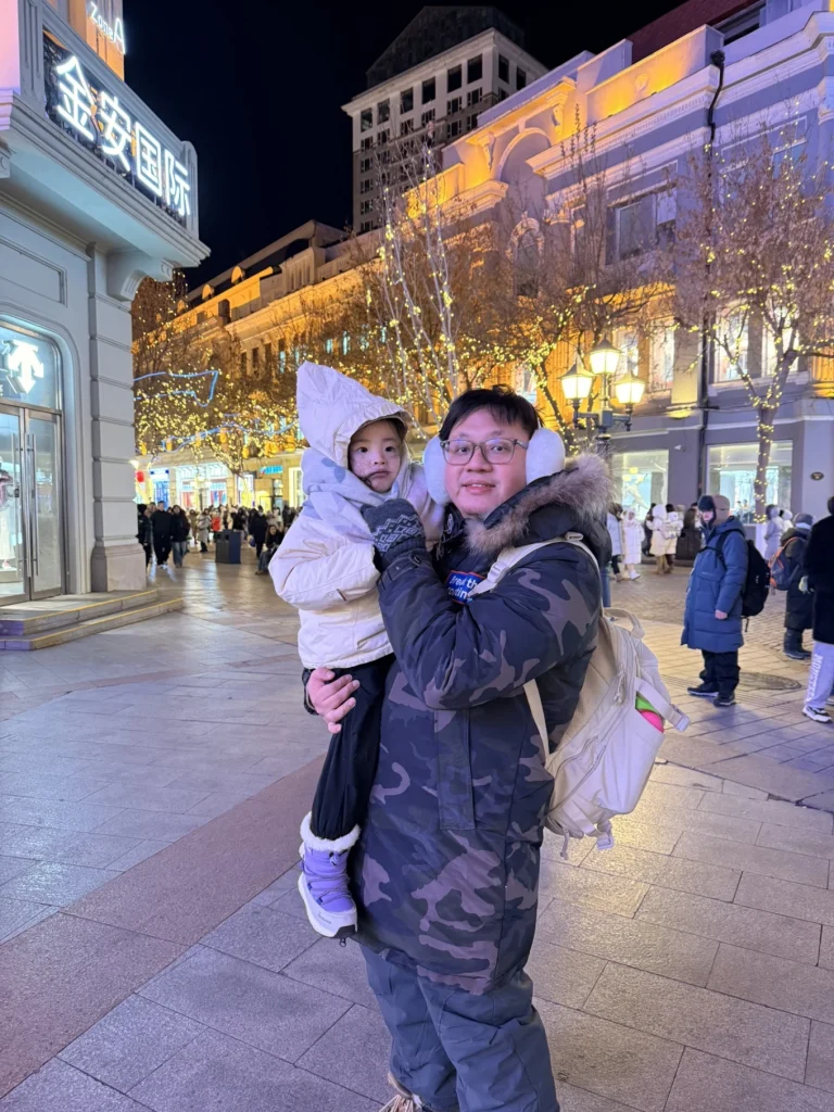 Parent holding a child on Central Street in Harbin at night with illuminated historic buildings in the background