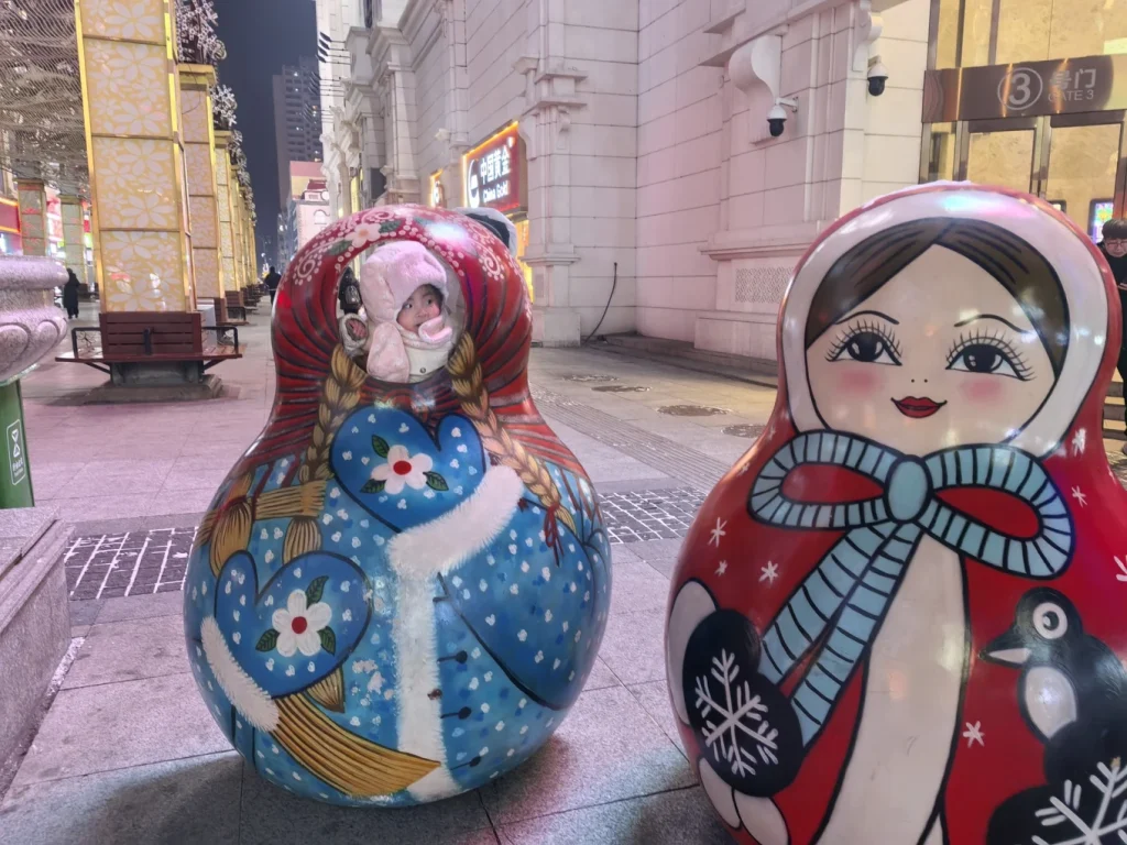 Child sitting inside a colorful matryoshka-style sculpture on Central Street in Harbin at night