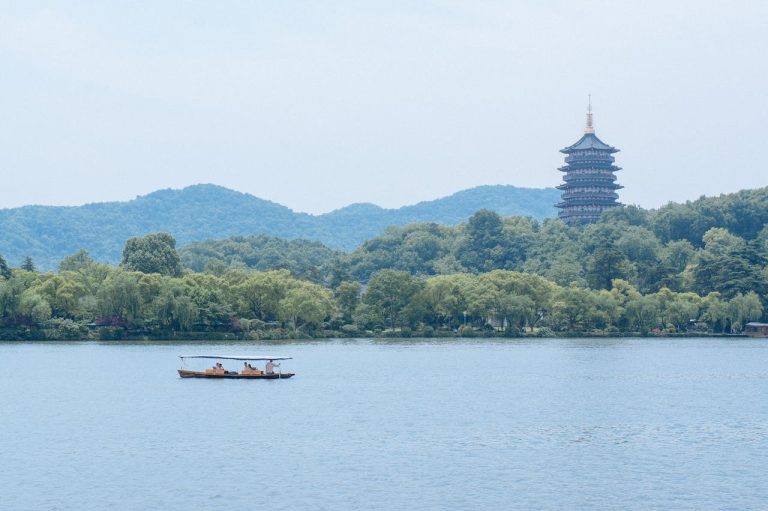 West Lake in Hangzhou with a traditional boat on the water and Leifeng Pagoda rising above the tree-lined hills
