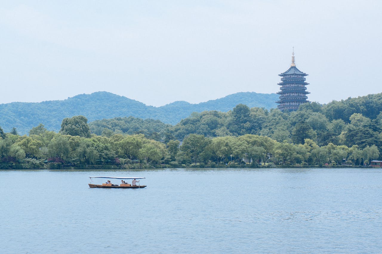 West Lake in Hangzhou with a traditional boat on the water and Leifeng Pagoda rising above the tree-lined hills