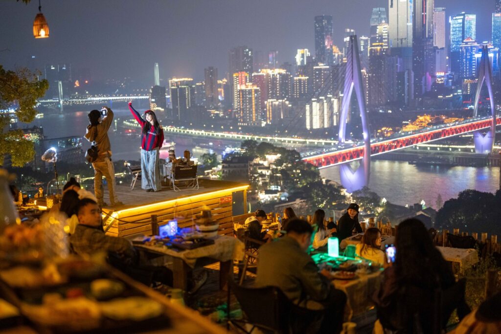 Rooftop bar in Chongqing overlooking illuminated bridge and skyline with diners enjoying river views at night
