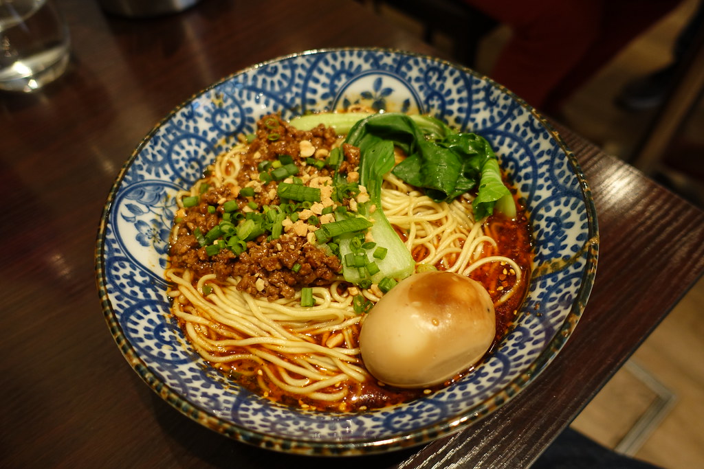 Chongqing Xiao Mian noodles with minced pork, chili oil broth, bok choy, scallions, peanuts, and braised egg in a traditional blue ceramic bowl
