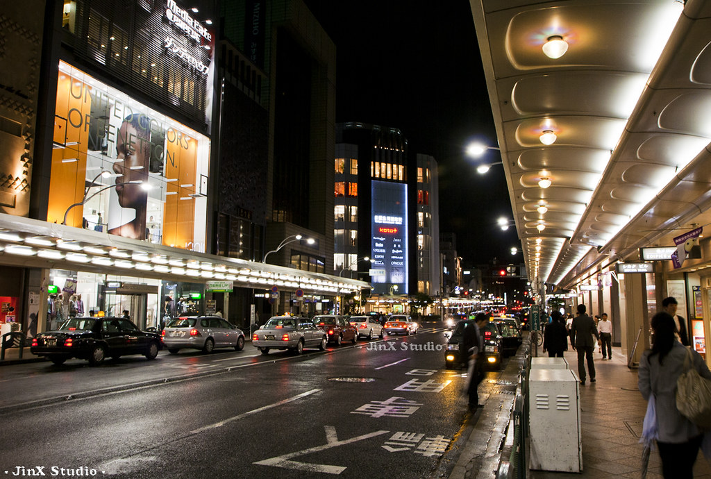 Night street scene in Nakagyo Ward Kyoto with illuminated storefronts, taxis, and covered pedestrian walkway in central Kyoto