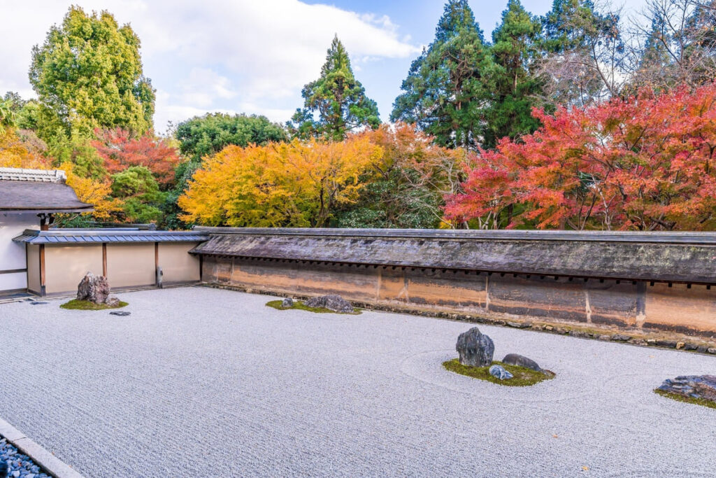 Best Japanese Temples to Visit: Top 6 Must-See Temples in Japan 9 Ryoan-ji Zen rock garden in Kyoto with carefully arranged stones on raked white gravel and colorful autumn trees in the background