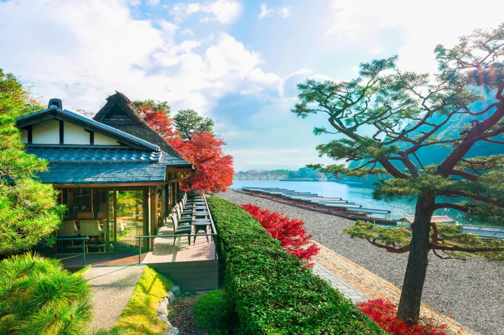 Suiran, a Luxury Collection Hotel, Kyoto terrace overlooking Arashiyama river with autumn maple trees and traditional architecture.