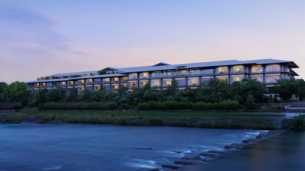 The Ritz-Carlton Kyoto exterior along the Kamogawa River at dusk with illuminated rooms and tranquil water reflections.