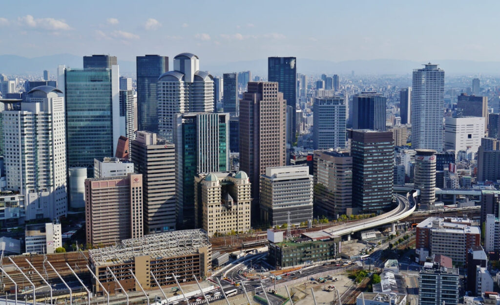 Osaka city skyline viewed from above, showing modern high-rise buildings and elevated highways in the Umeda district on a clear day.
