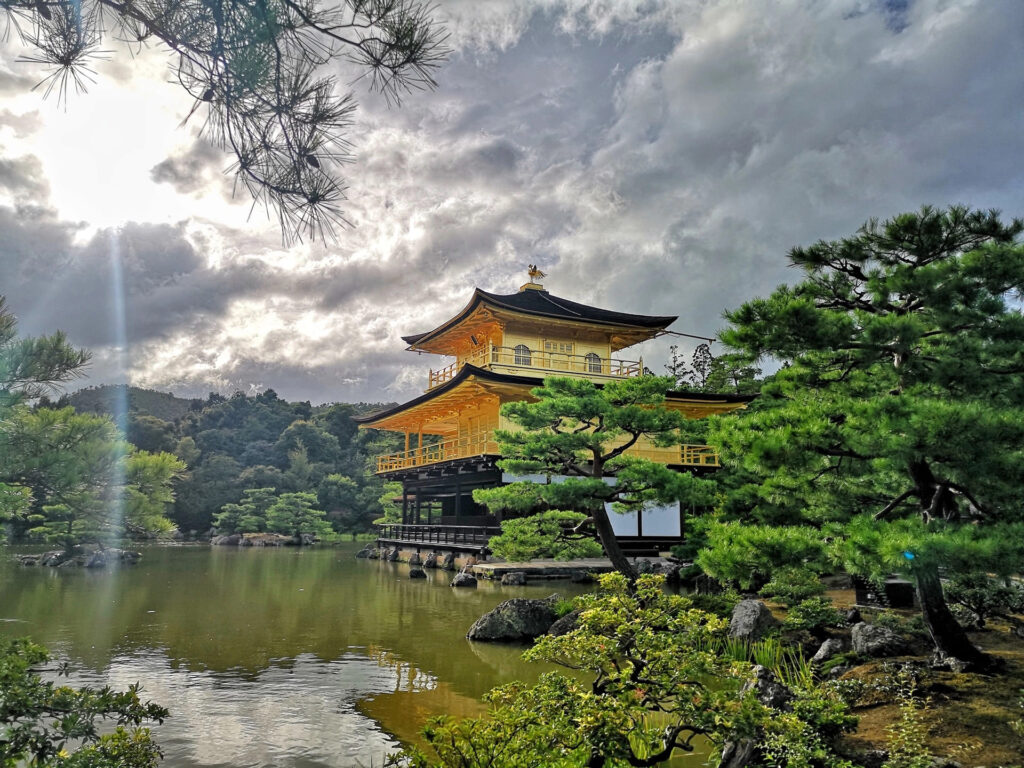 Golden Temple Kyoto Guide: Kinkaku-ji Travel Tips & History 8 Golden Temple Kyoto (Kinkaku-ji) glowing under dramatic cloudy sky with sun rays reflecting on Mirror Pond