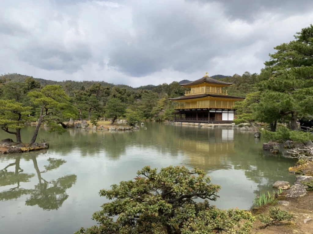 Golden Temple Kyoto Guide: Kinkaku-ji Travel Tips & History 6 Wide landscape view of Golden Temple Kyoto across Mirror Pond with lush greenery and mountains