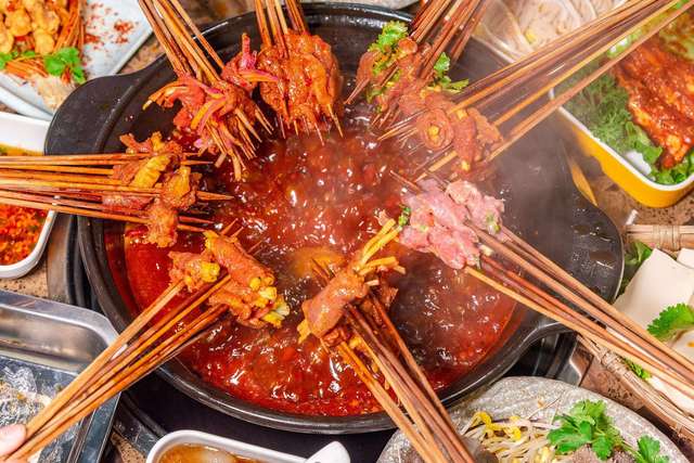 Chuan Chuan Xiang skewers cooking in spicy Chongqing málà broth with chili oil and Sichuan peppercorns