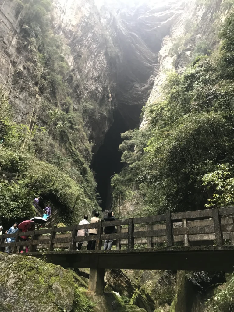 Visitors standing on wooden bridge inside towering limestone gorge at Wulong Karst National Park