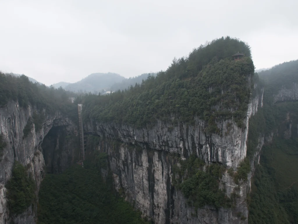 Visitors walking along cliffside path inside the Three Natural Bridges sinkhole in Wulong Karst Chongqing