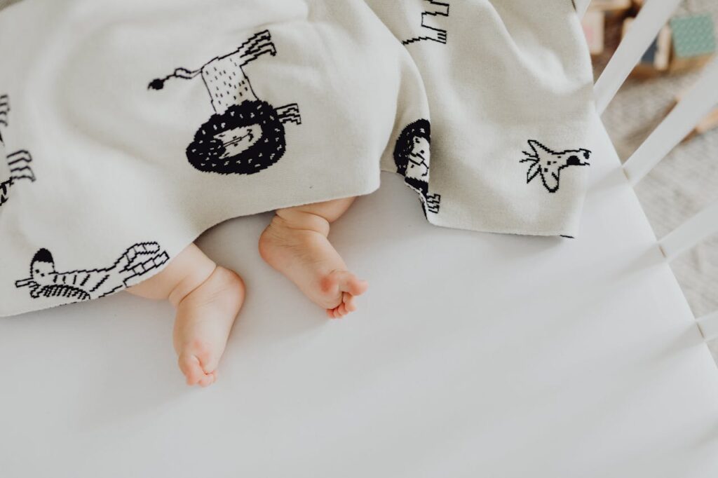 Baby’s feet sticking out from under a soft patterned blanket in a crib