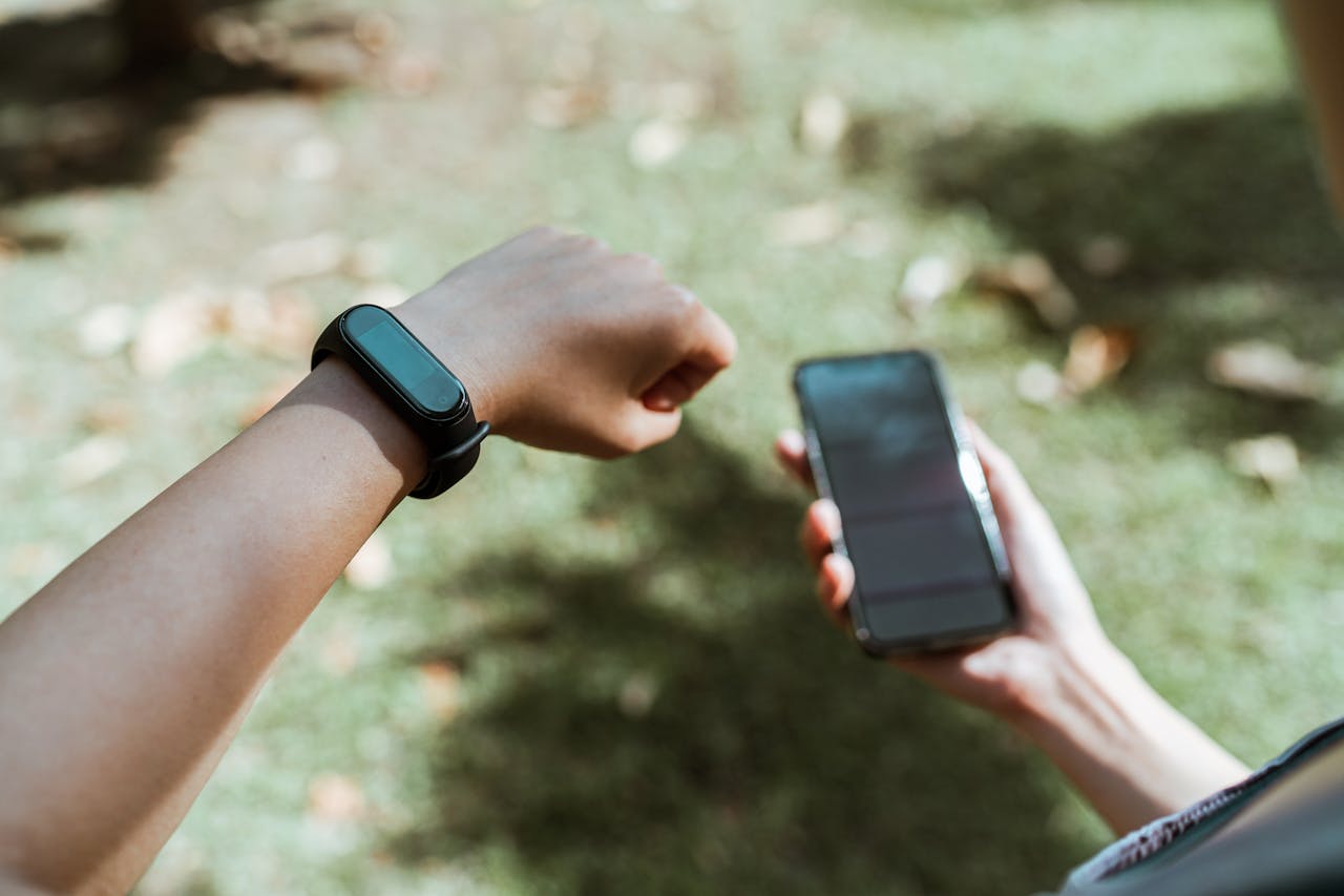 Parent checking a GPS smartwatch tracker on a child’s wrist while holding a smartphone outdoors