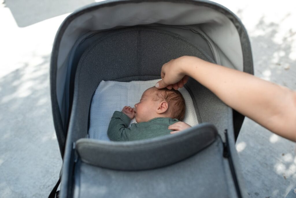 Baby sleeping peacefully in a stroller while a parent gently touches the baby's head