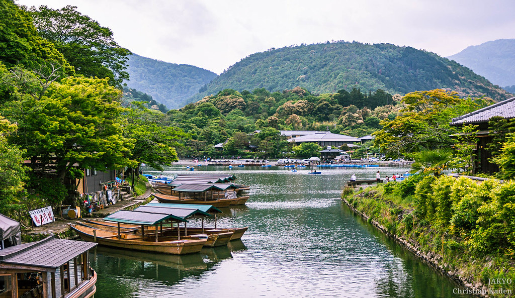 Arashiyama Kyoto river with traditional boats, lush greenery, and mountains in the background
