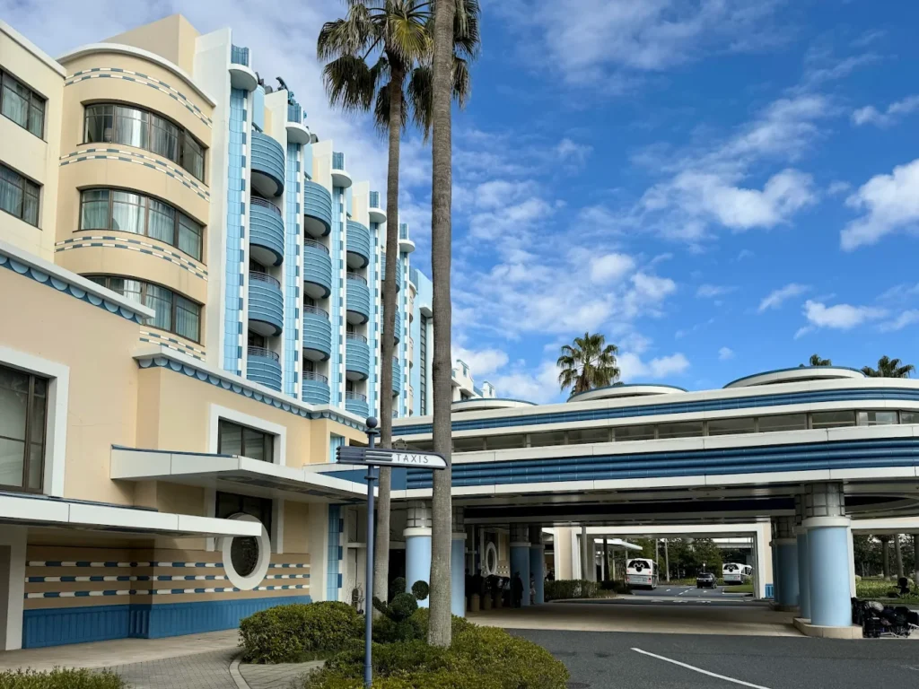 Exterior of Disney Ambassador Hotel with Art Deco design, blue accents, palm trees, and entrance driveway