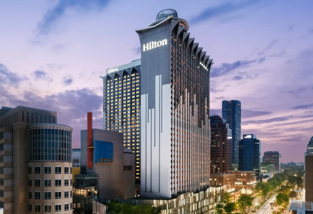 Hilton Singapore Orchard hotel exterior at sunset along Orchard Road with city skyline and modern high-rise architecture