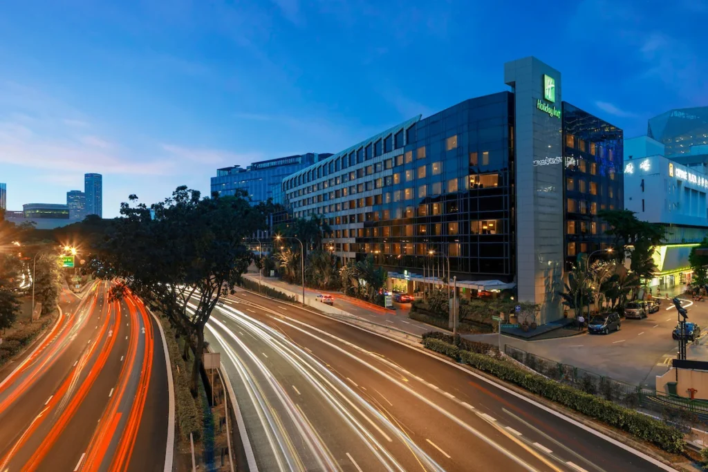 Holiday Inn Singapore Orchard City Centre hotel exterior at night along Orchard Road with city traffic lights and urban skyline